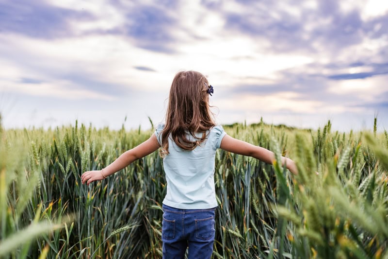 A little girl walking throeugh a field.