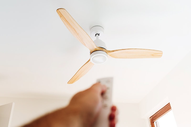 How to Choose the Right Ceiling Fan for Your Space. A person using a remote to control a fan.