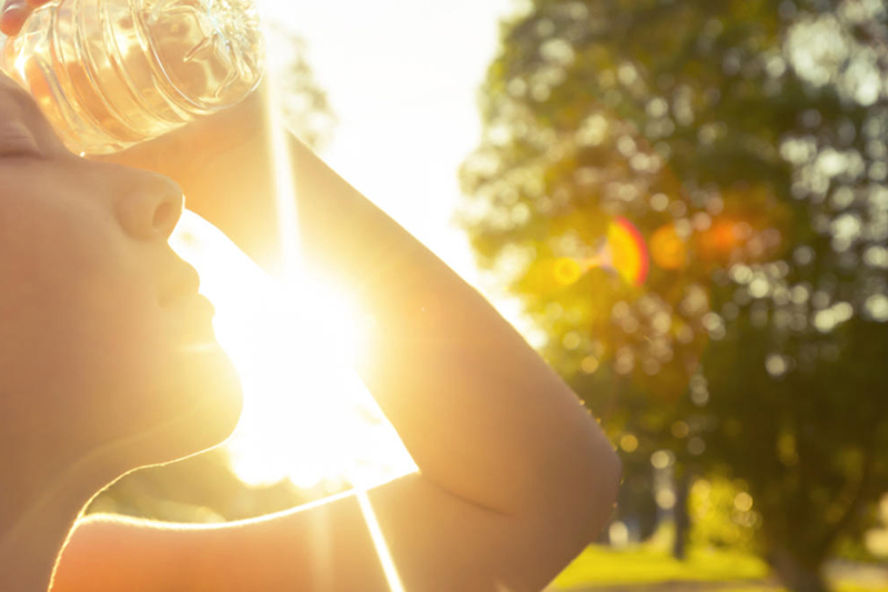 Prepare for Hot Weather With an Air Conditioning Tune-up. Photo of a woman in the sun, trying to cool off with a water bottle.